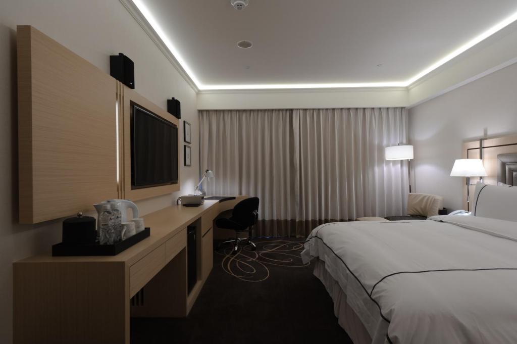 a hotel room with a bed and a desk with a television at K Hotel Taipei Songjiang in Taipei