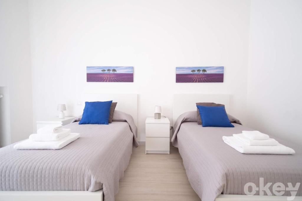 2 Betten in einem weißen Zimmer mit blauen Kissen in der Unterkunft Casa Viviana - Bari Policlinico in Bari
