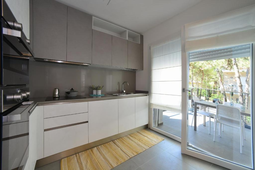a kitchen with white cabinets and a sliding glass door at Residence Due Perle in Lignano Sabbiadoro