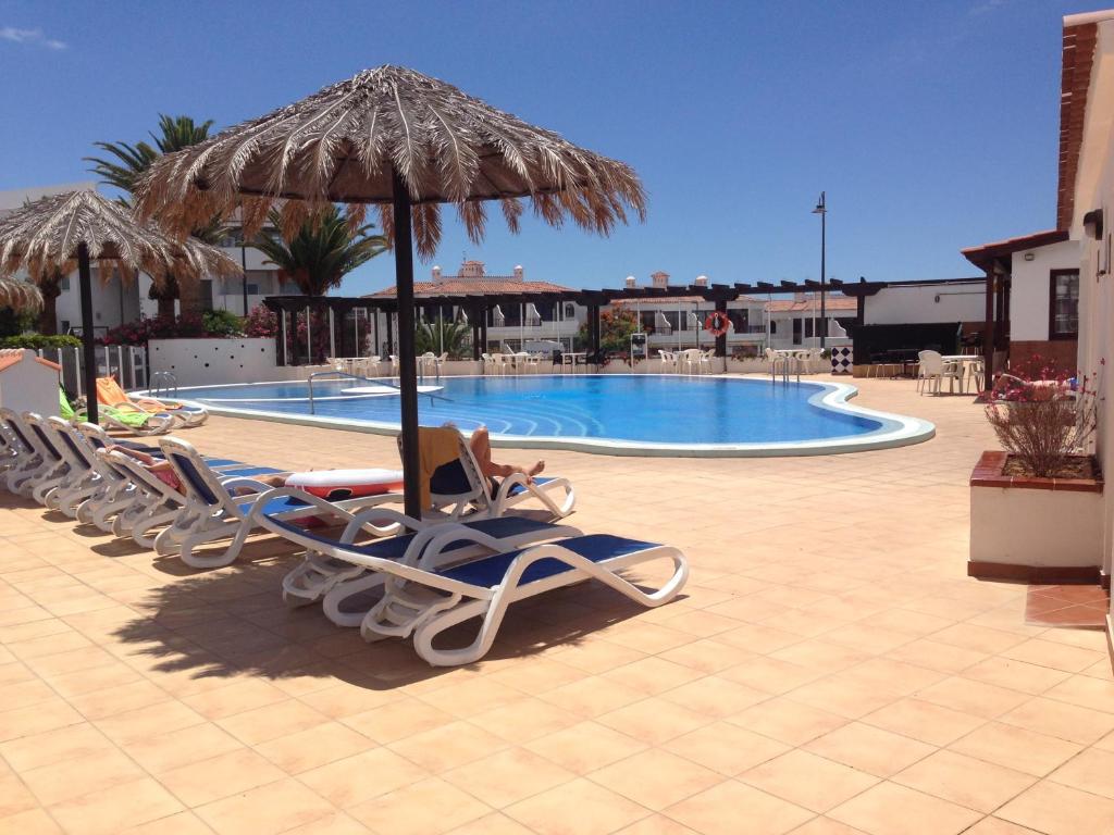 un grupo de sillas y una sombrilla junto a la piscina en Apartamento La Palmera Amarilla Golf, en San Miguel de Abona