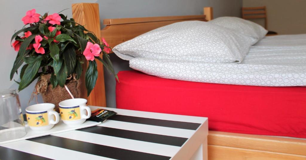 a bed with two coffee cups and a table with flowers at Liepu Hostelis in Liepāja