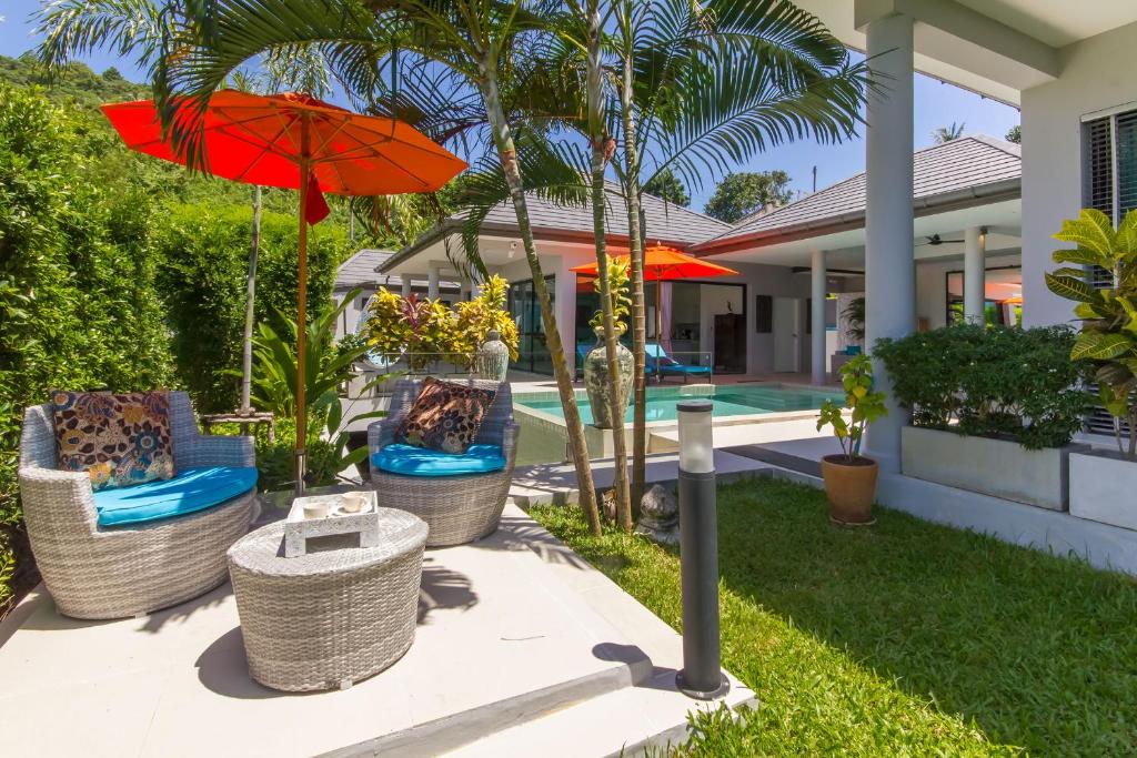 a patio with chairs and an umbrella and a pool at Villa Tropical Cocoon in Koh Samui 