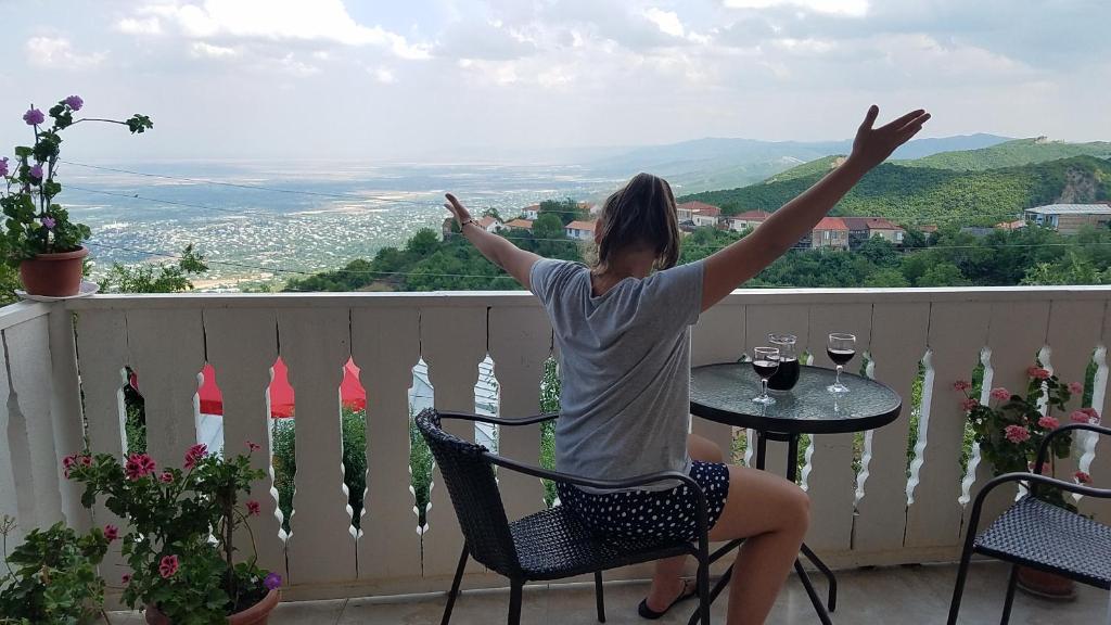 a woman sitting at a table on a balcony with her arms up at Guest House Maria in Sighnaghi