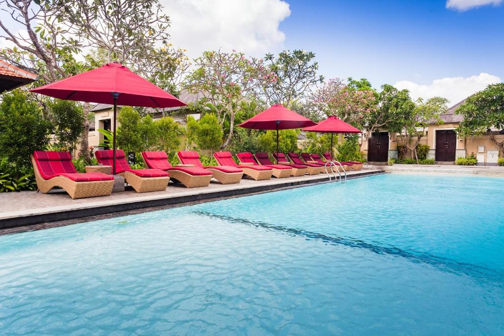 a swimming pool with red umbrellas and chairs and a pool at Aldeoz Grand Kancana Villas Resort Bali in Kerobokan