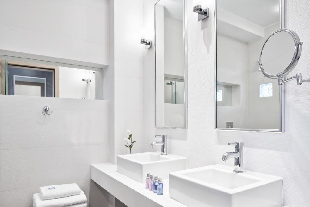 a white bathroom with two sinks and mirrors at Antigoni Seaside Resort in Ormos Panagias