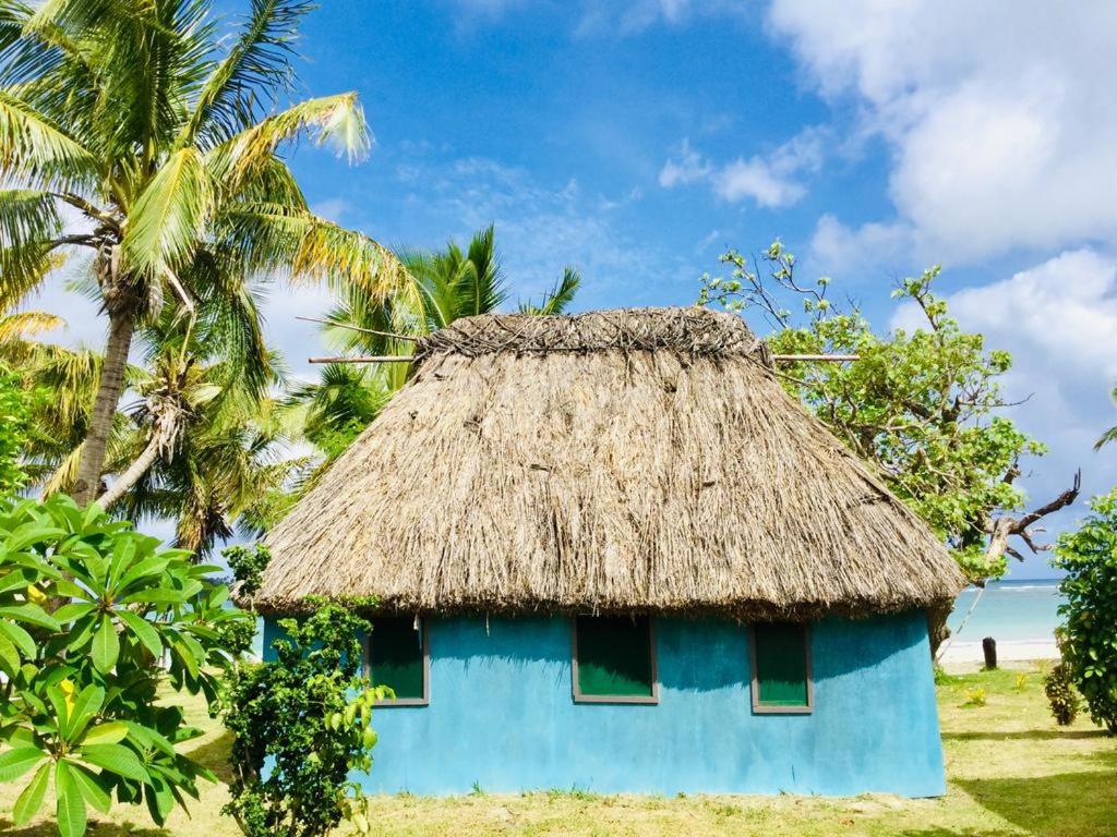 Nacula Island的住宿－Malakati Village Beach House，蓝色房子,拥有茅草屋顶和棕榈树
