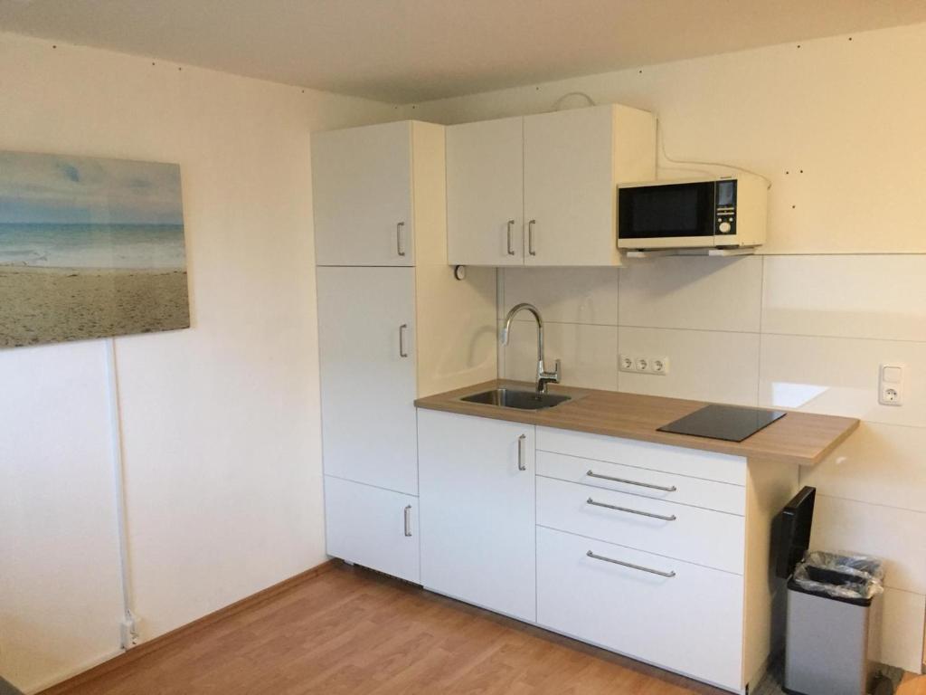 eine Küche mit weißen Schränken, einer Spüle und einer Mikrowelle in der Unterkunft Strandnest in Horumersiel