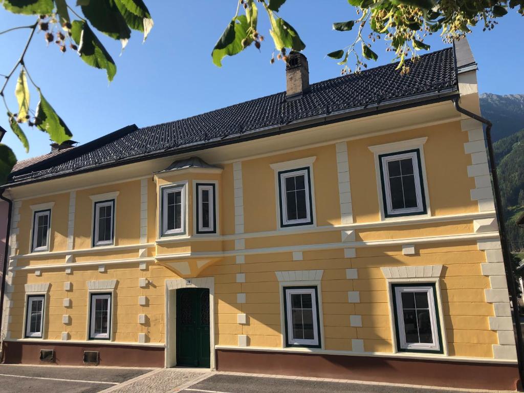 een geel huis met een zwart dak bij Ferienwohnungen Appartementhaus Hohe Tauern in Obervellach