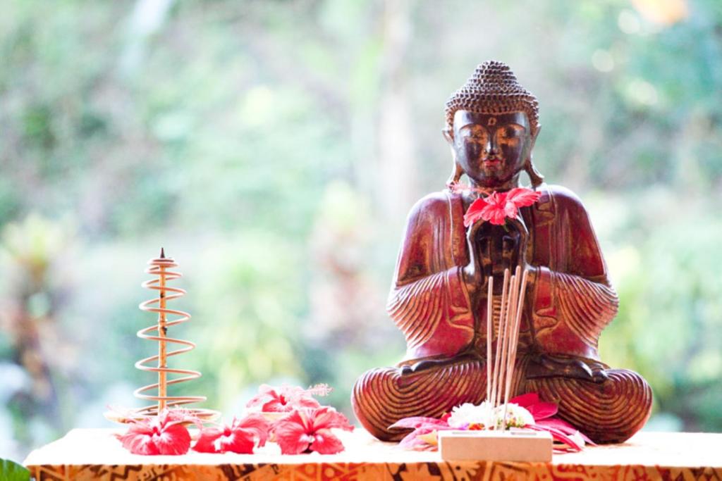 uma estátua de um Buda sentado numa mesa com flores em Gaia-Oasis Mountain Abasan em Tejakula