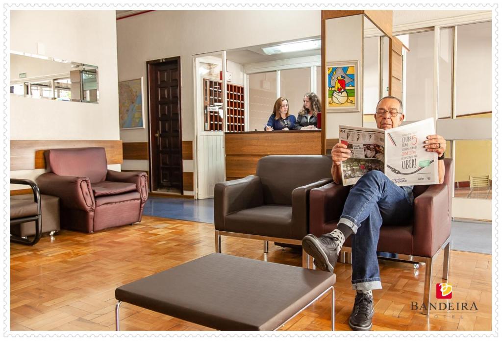 a man sitting in a chair reading a newspaper at Bandeira Hotel in Caxias do Sul