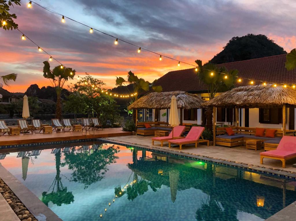 a swimming pool with chairs and a house with a sunset at The Banana Tree Hostel in Ninh Binh