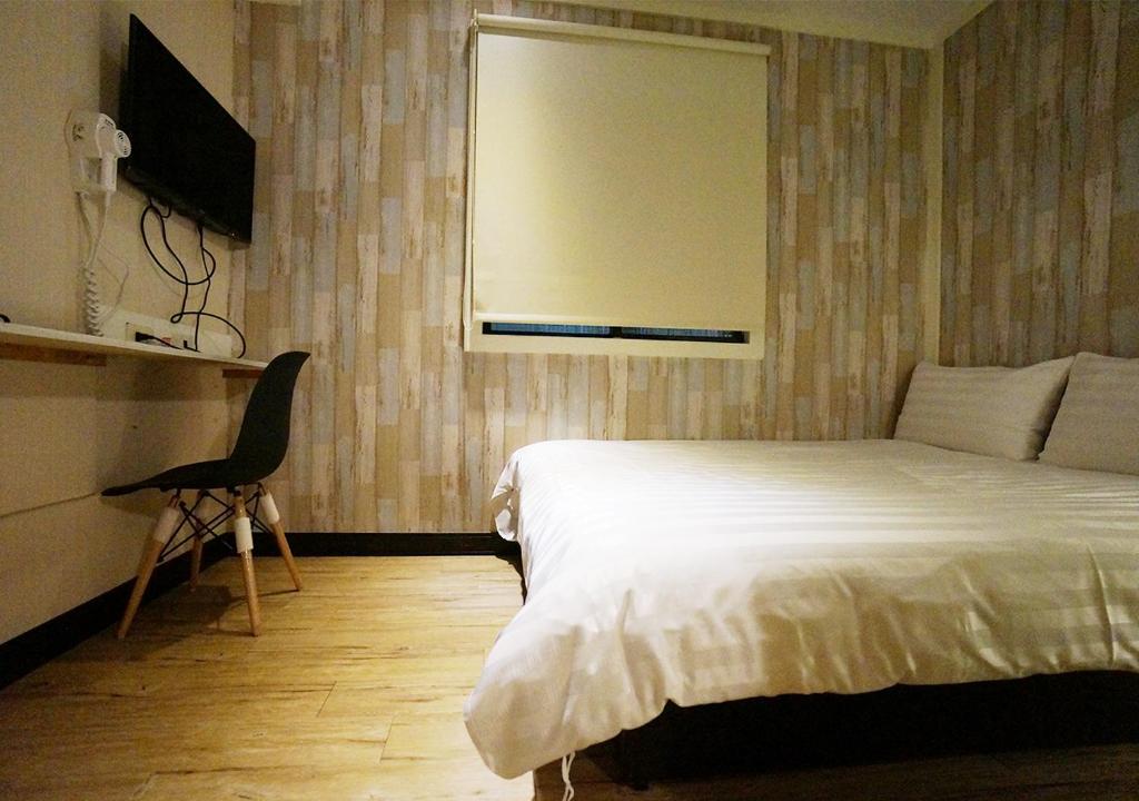 a bedroom with a bed and a chair and a window at Win Inn Kaohsiung Hotel in Kaohsiung