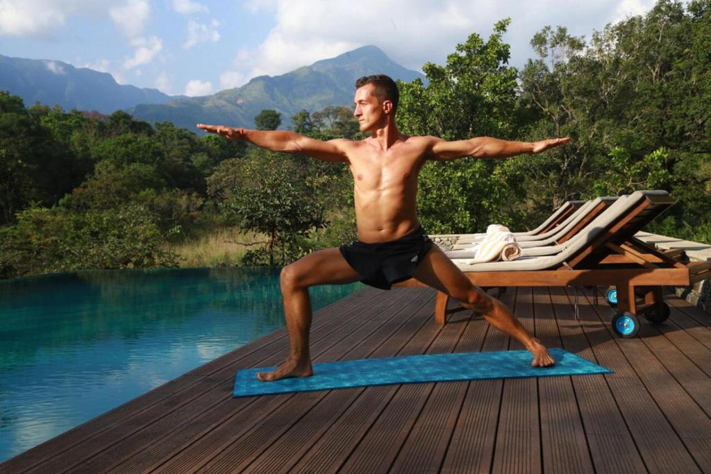 un hombre haciendo una pose de yoga en una esterilla de yoga junto a una piscina en Sennya Resorts, en Belihuloya