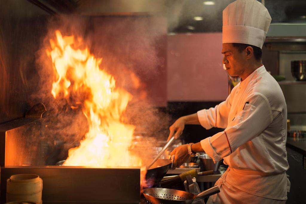 a chef cooking on a grill with flames at The Berkeley Hotel Pratunam in Bangkok