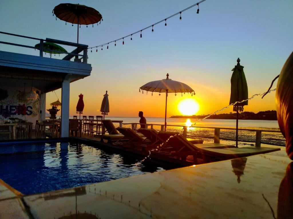 a pool with chairs and umbrellas and the sunset at Rumah Marta Ceningan Island in Nusa Lembongan
