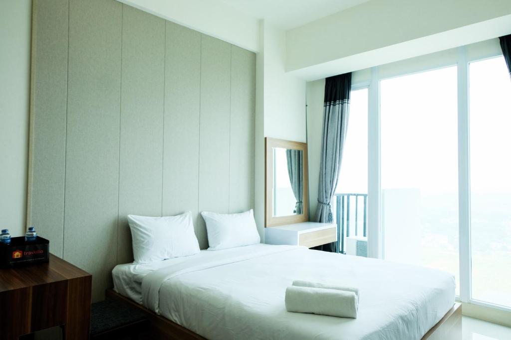 a bedroom with a large white bed with a window at Homey Studio Room Tree Park City BSD Apartment near BSD City By Travelio in Tangerang