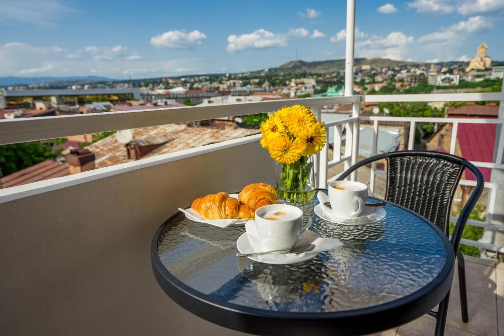 提比里斯的住宿－Hotel Imperial House，阳台上的桌子上配有咖啡杯和羊角面包