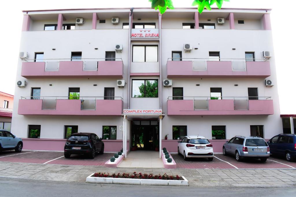 a pink and white building with cars parked in a parking lot at Complex Fortuna in Eforie Sud