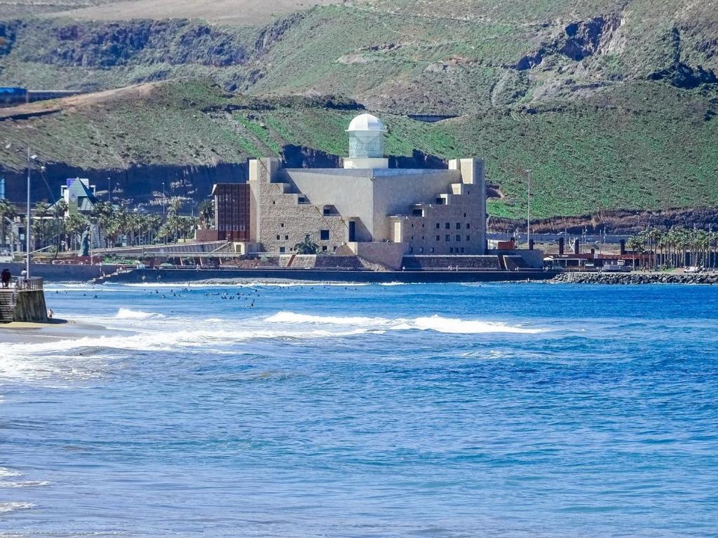 a building with a lighthouse on the beach next to the water at Casa Las Canteras in Las Palmas de Gran Canaria