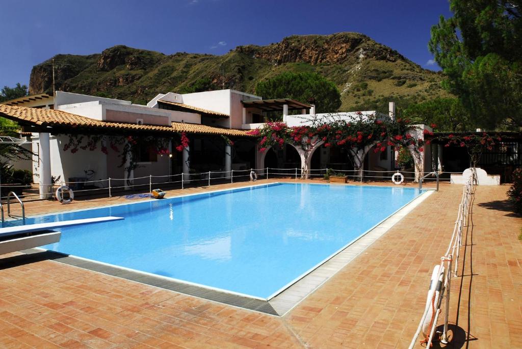 a large blue swimming pool with a mountain in the background at Villa Saracina in Vulcano