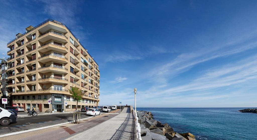 a building next to the ocean with cars parked next to it at Hotel Parma in San Sebastián