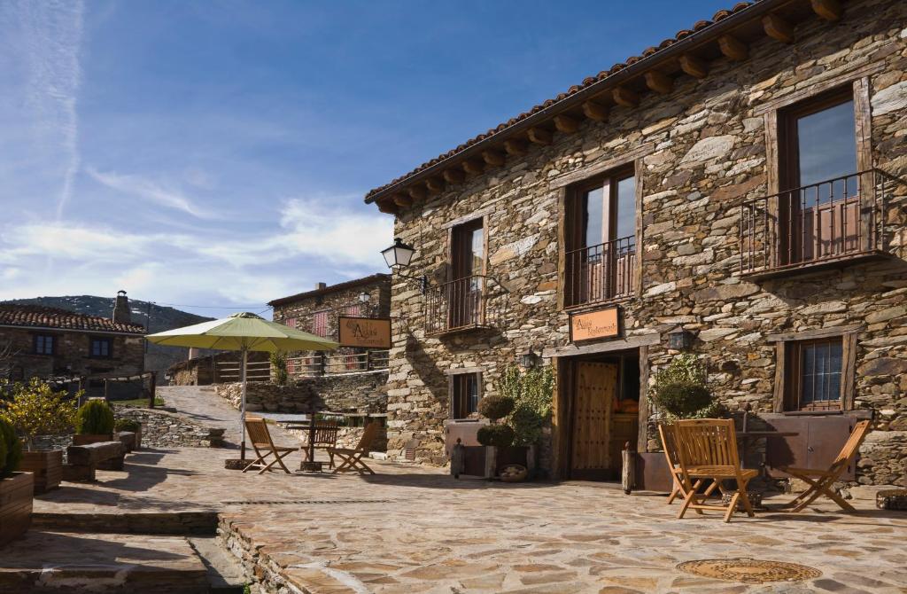 a stone building with chairs and an umbrella at CASA ALDABA in La Hiruela