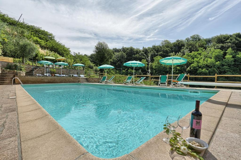 a swimming pool with umbrellas and chairs and a bottle of wine at Borgo di Alica in Palaia