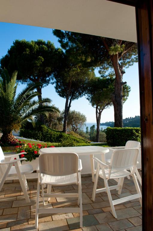 a patio with white chairs and a table and trees at Villa Anna Maria in Agia Paraskevi