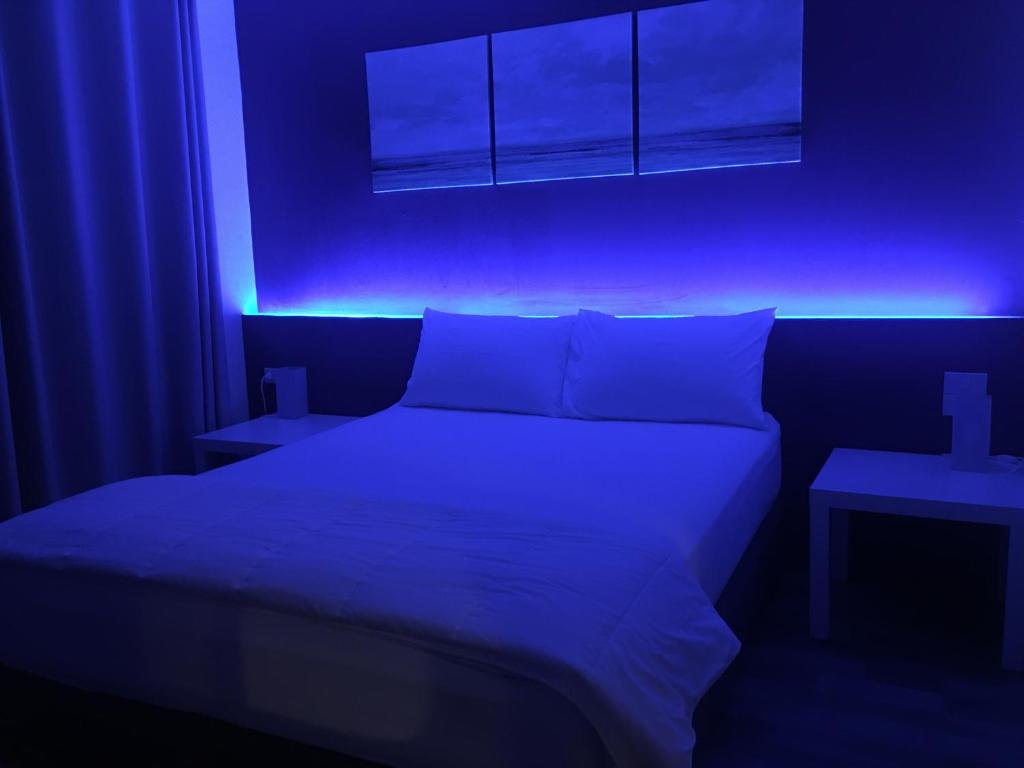 A bed is framed by intense blue LED lighting in a dark, atmospheric bedroom.
