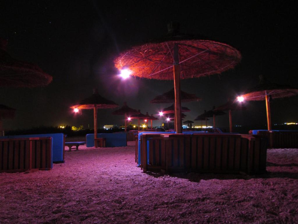 a beach with tables and umbrellas at night at Blue Paradise Hotel in Orikum