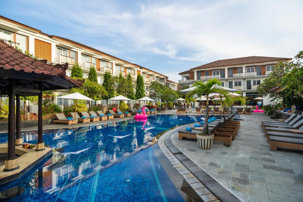 una piscina en un hotel con sillas y sombrillas en Kuta Beach Club Hotel, en Kuta