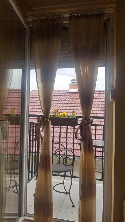 een glazen schuifdeur met gordijnen op een balkon bij Soba 205 in Vrnjačka Banja