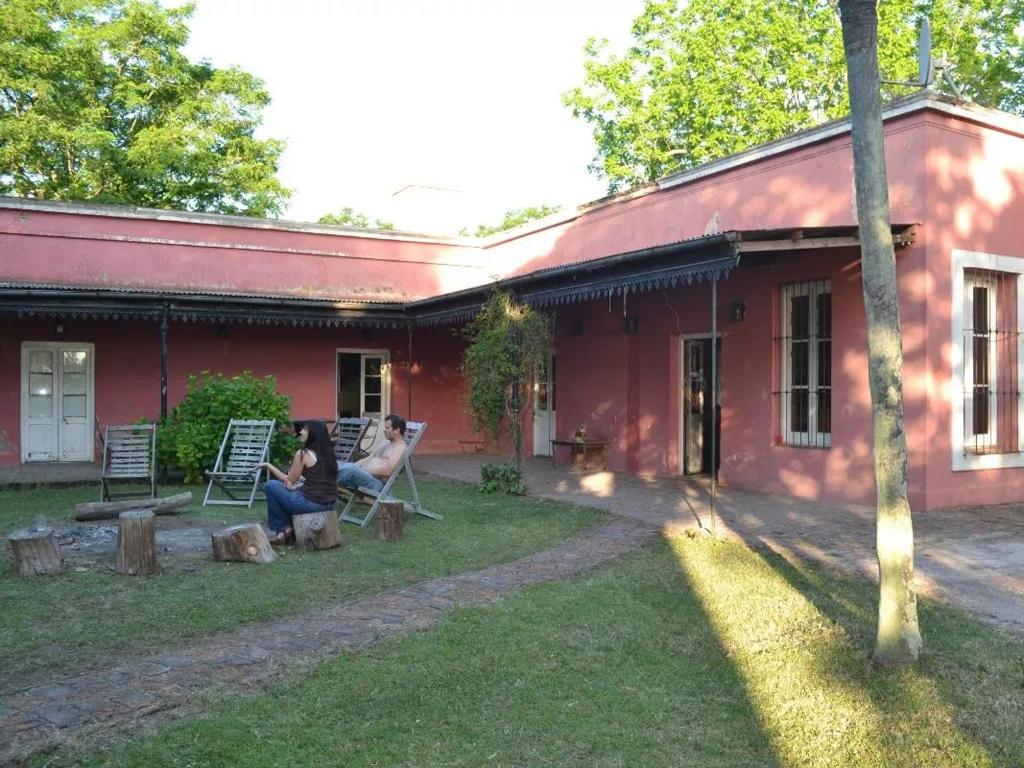 twee mensen in stoelen buiten een rood huis bij La Rosadita Casa de Campo in Chascomús