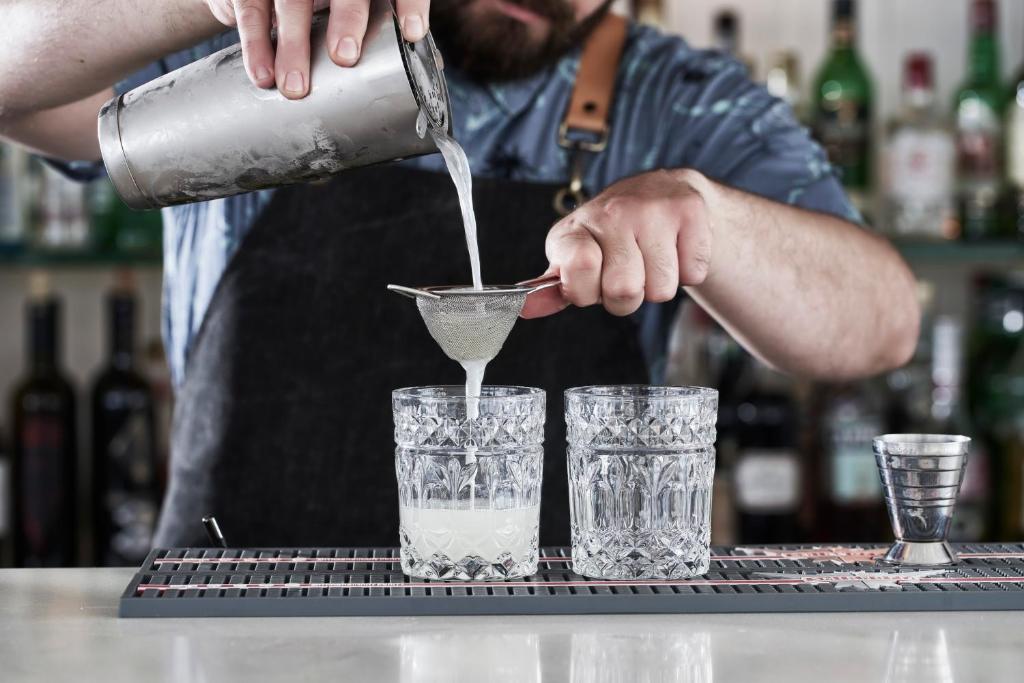 a man pouring a drink into two glasses on a bar at Antigoni Seaside Resort in Ormos Panagias