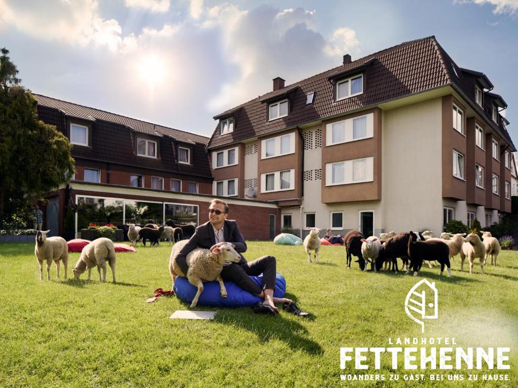a man sitting on the grass with a sheep at Landhotel Fettehenne in Leverkusen