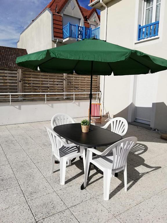 une table et des chaises noires avec un parasol vert dans l'établissement Vie de famille, à Sainte-Cécile-Plage