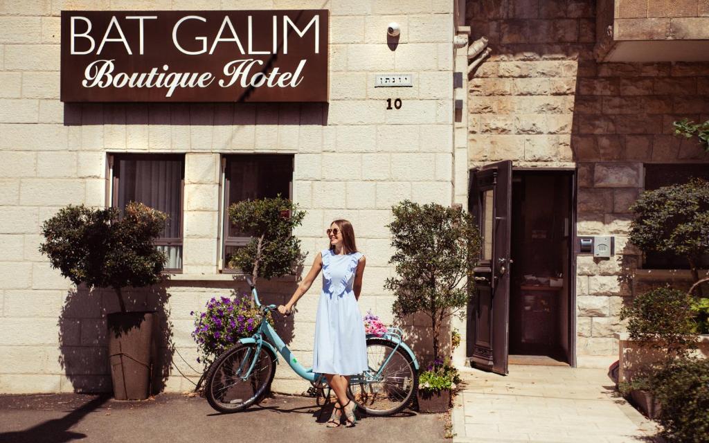 een vrouw in een witte jurk die naast een fiets staat bij Bat Galim Boutique Hotel in Haifa