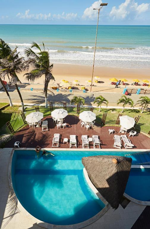 a swimming pool next to a beach with chairs and umbrellas at Elegance Comfort Natal Beira mar Coberturas Vip in Natal