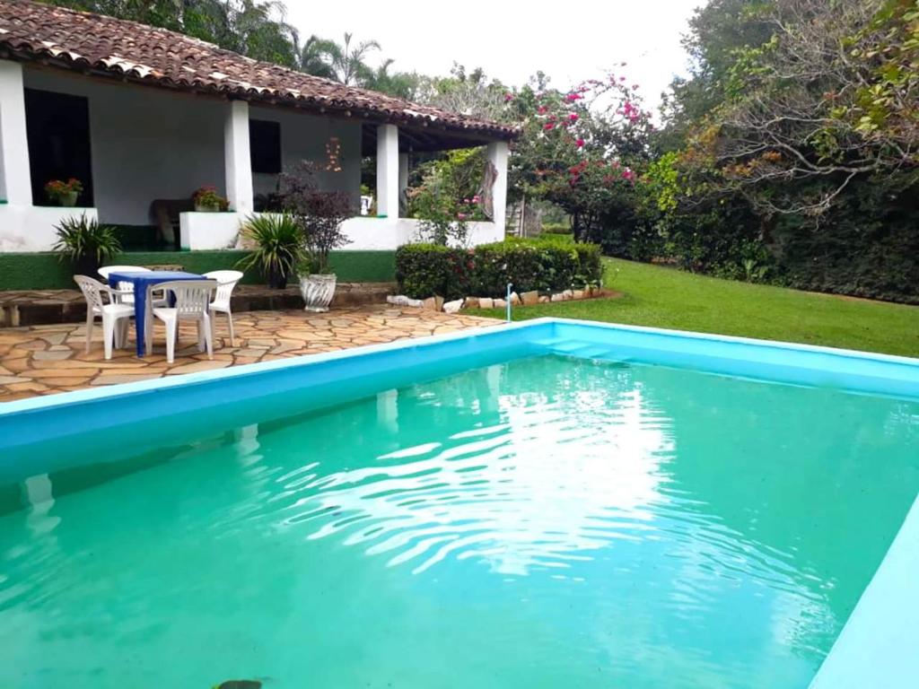 a pool in front of a house with a table and chairs at Chacara bica dágua in Pirenópolis