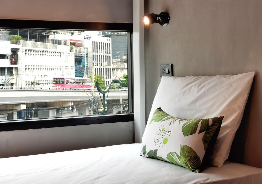 a bed with a pillow in front of a window at Siam Eco Hostel in Bangkok