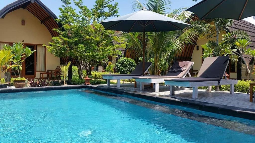 a swimming pool with two chairs and an umbrella at Bedolo Bungalows in Gili Islands