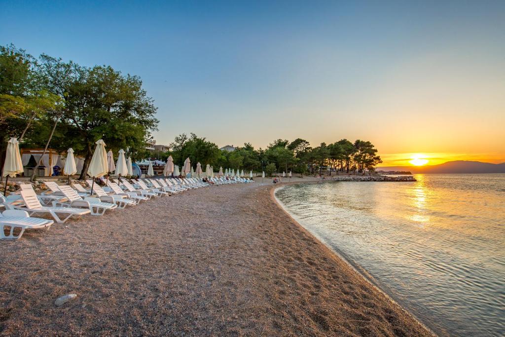 a beach with chairs and umbrellas at sunset at Blue Waves Resort in Malinska
