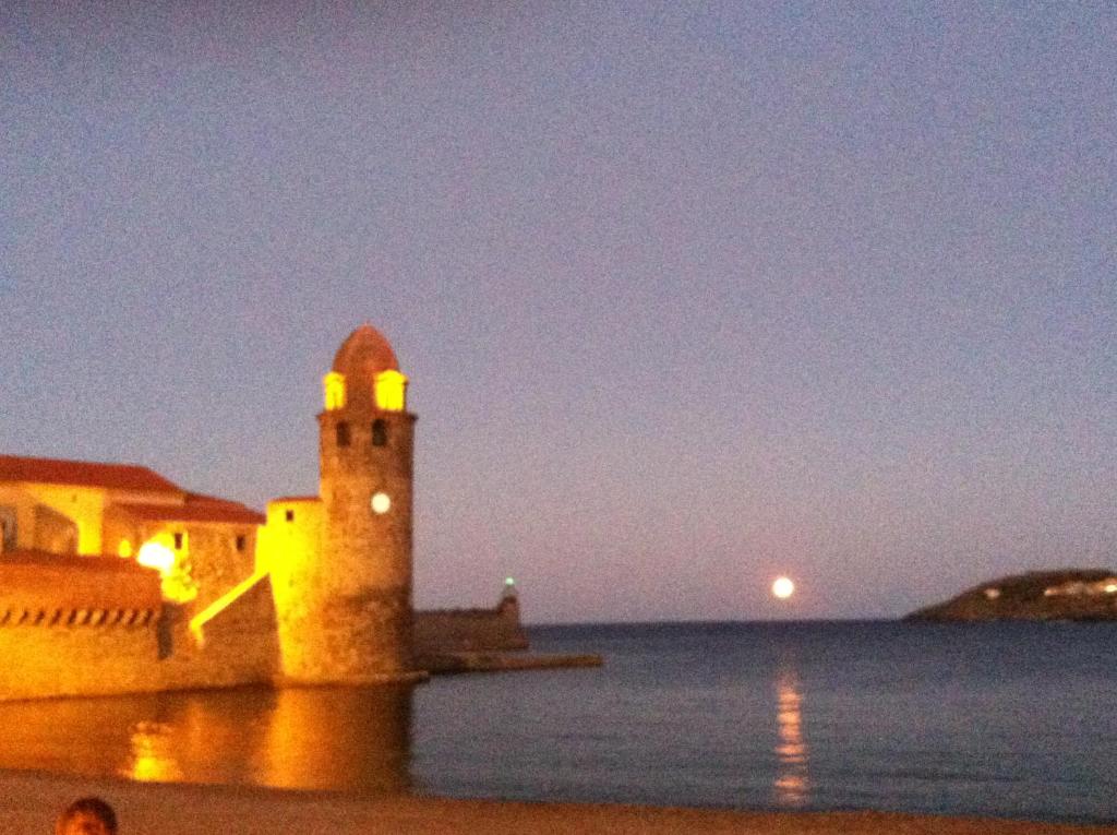 a lighthouse on the beach with the moon in the background at Collioure in Collioure