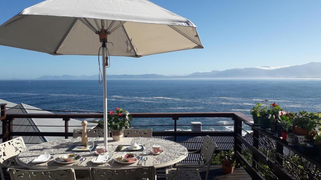 uma mesa com um guarda-chuva numa varanda com o oceano em Eirene Place em De Kelders