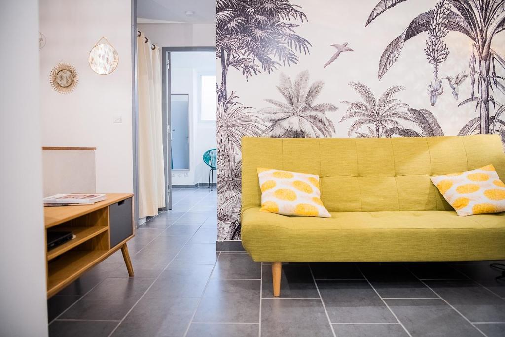 ein gelbes Sofa in einem Wohnzimmer mit Palmtapete in der Unterkunft Appartement Denim in Nîmes