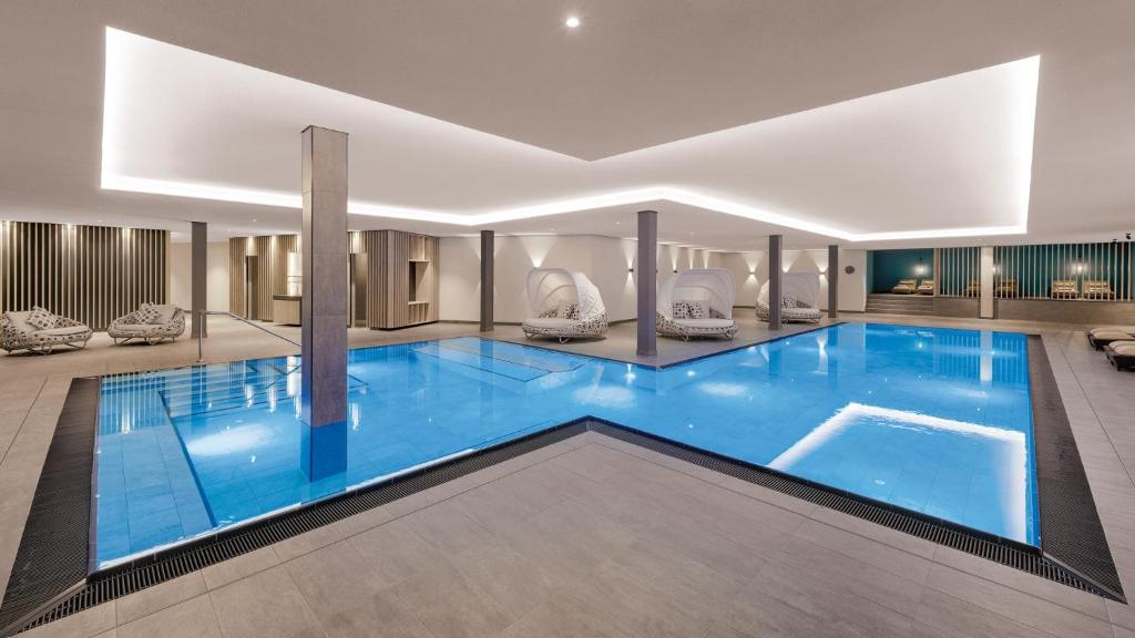 a large blue pool in a building with chairs around it at Hotel Traube am See in Friedrichshafen