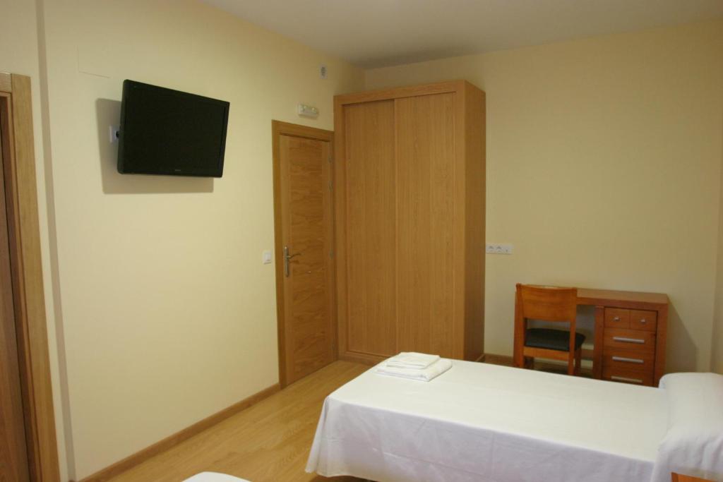 a bedroom with two beds and a television on the wall at Albergue La Encina in Hospital de Órbigo