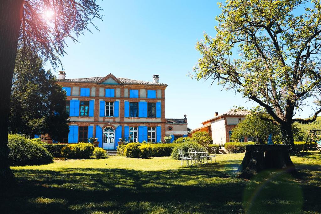 une grande maison avec des fenêtres bleues dans un parc dans l'établissement La Maison du Saula, à Lafrançaise