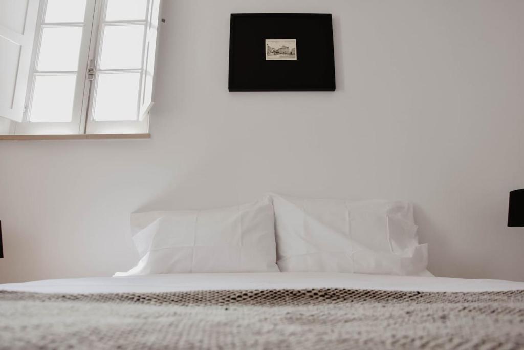 een slaapkamer met witte muren en een bed met witte kussens bij Apartamento acolhedor e elegante em prédio típico - Self check in in Coimbra