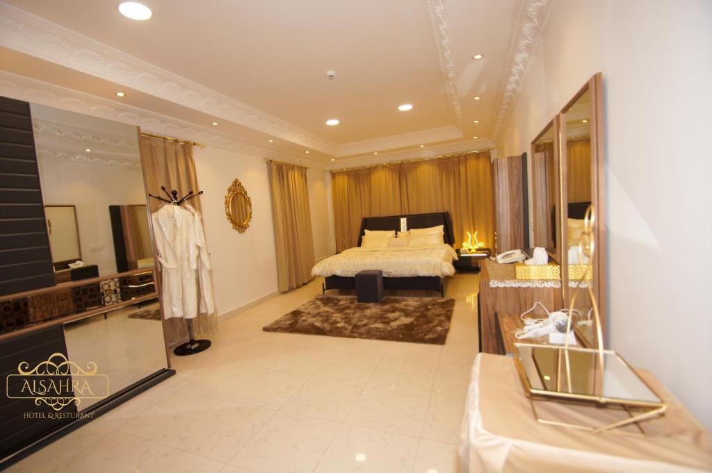 een grote slaapkamer met een bed en een spiegel bij ALSAHRA Belshamal Hotel in Rafha